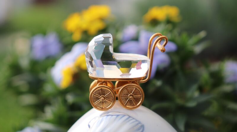 baby carriage, crystal figurine, gold decoration, new baby, baby shower, elegant gift, miniature pram, baby symbol, celebration, motherhood, birth announcement, decorative item, sparkling crystal, golden wheels, delicate ornament, baby theme, floral background, macro shot, close up, keepsake, luxury detail, gift idea, new life, parenting, baby celebration